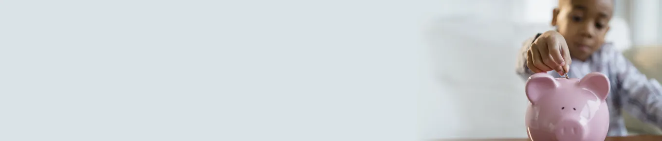 small boy adding money to a piggy bank